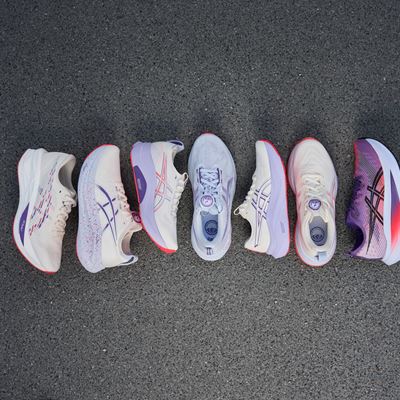 A top-down view of six pairs of running shoes arranged in a row on a gray asphalt surface, featuring various shades of white, purple, and pink with different designs and patterns.