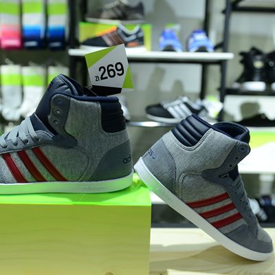 A pair of gray high-top sneakers with red stripes displayed on a green pedestal in a retail store. The price tag reads "269." In the background, various other shoes and socks are visible on shelves.