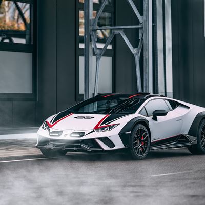 A sleek, modern sports car with a white and black exterior featuring red accents, parked on a city street. The car is surrounded by a misty atmosphere, showcasing its aerodynamic design and aggressive styling against a backdrop of industrial architecture.